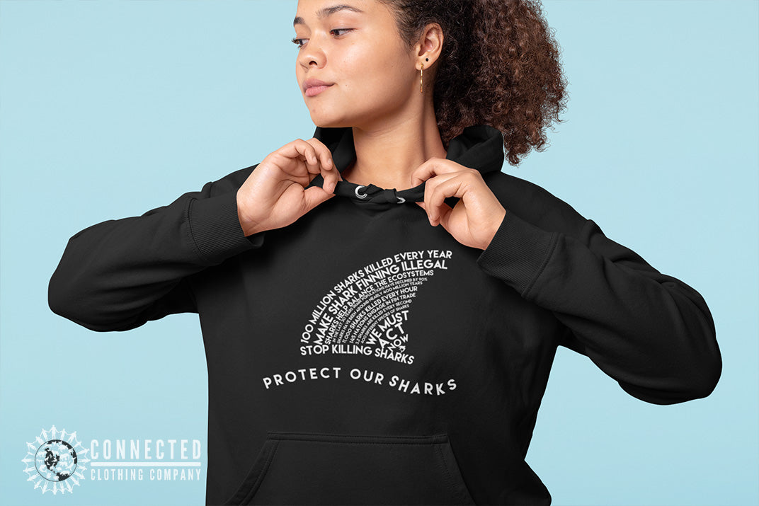 Model wearing black Protect Our Sharks Unisex Hoodie in front of blue backdrop - sharonkornman - Ethically and Sustainably Made - 10% donated to Oceana shark conservation