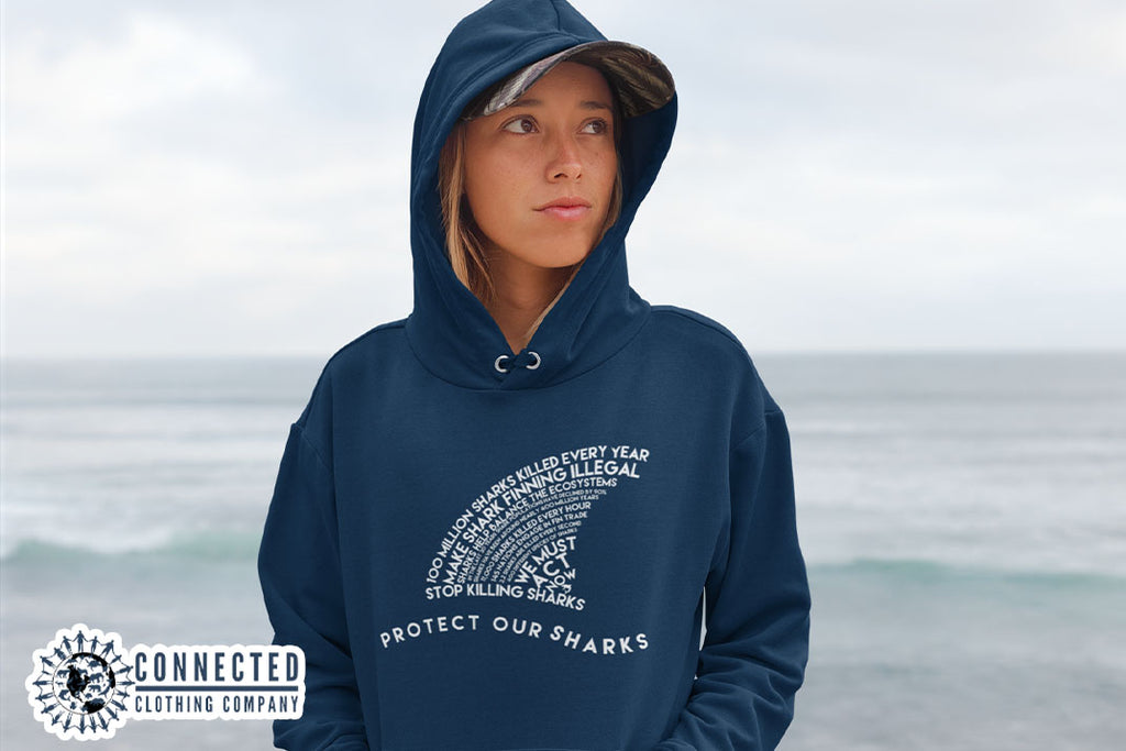 woman on the beach wearing navy blue Protect Our Sharks Unisex Hoodie - sharonkornman - Ethically and Sustainably Made - 10% donated to Oceana shark conservation