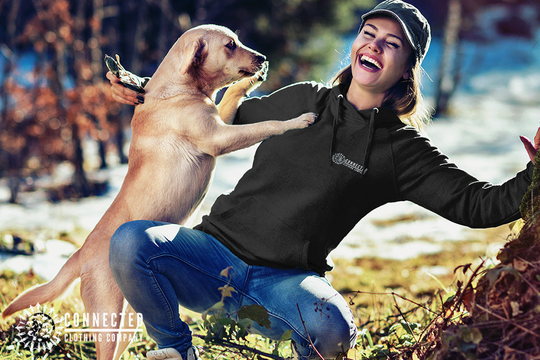 Model wearing Black Show Humanity Unisex Hoodie while smiling and playing with a rescue dog - sharonkornman - Ethically and Sustainably Made - 10% donated to the Society for the Prevention of Cruelty to Animals